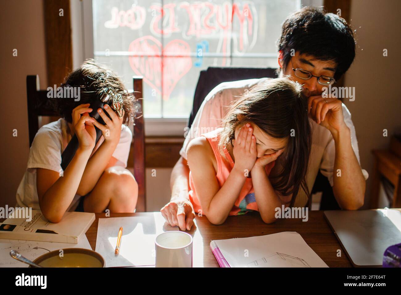 due bambini infelici con la testa in mano siedono con stanchi padre a tavola Foto Stock