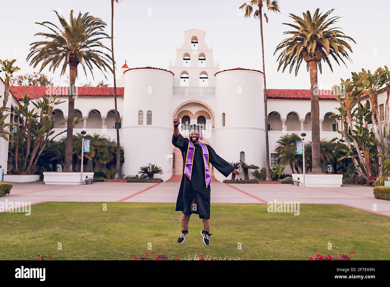 Uomo che salta, indossando un abito/berretto di laurea all'università. Foto Stock
