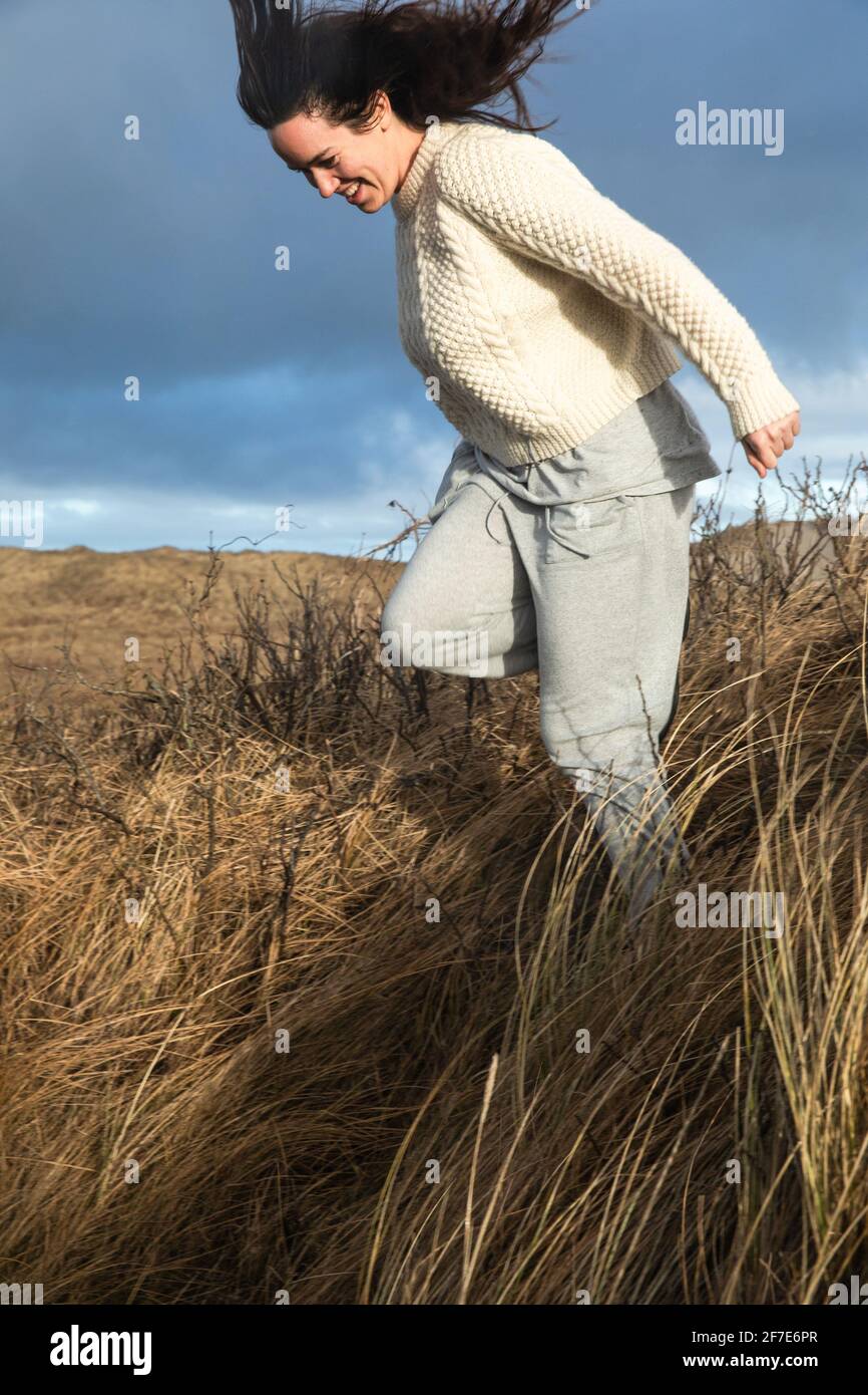 Donna che corre giù Hill con Tall Grass come il vento Colpi in Danimarca Foto Stock