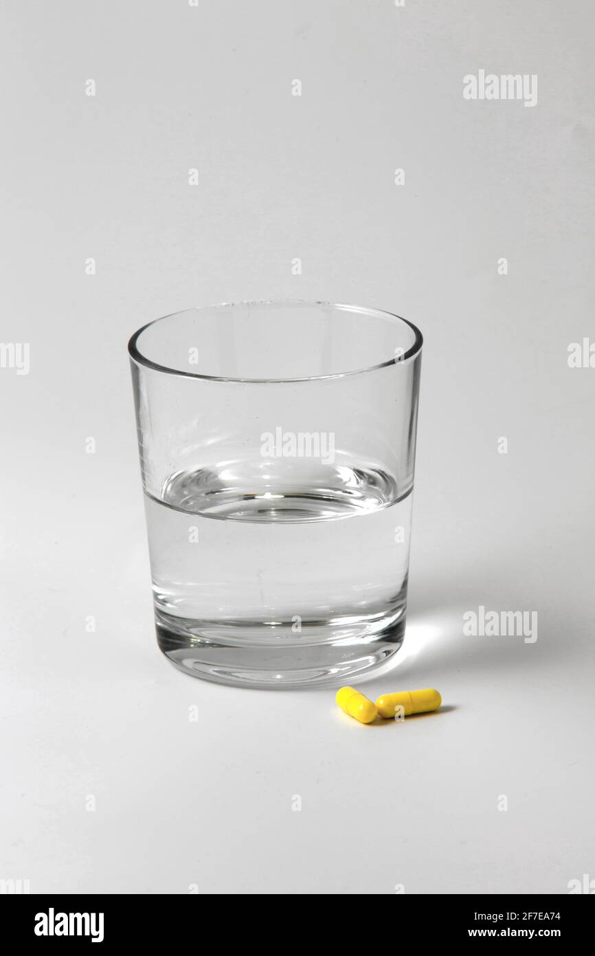 Immagine di un bicchiere d'acqua e di due compresse pronte per essere prese su uno sfondo bianco con spazio per la copia. Medicina e farmaci. Foto Stock