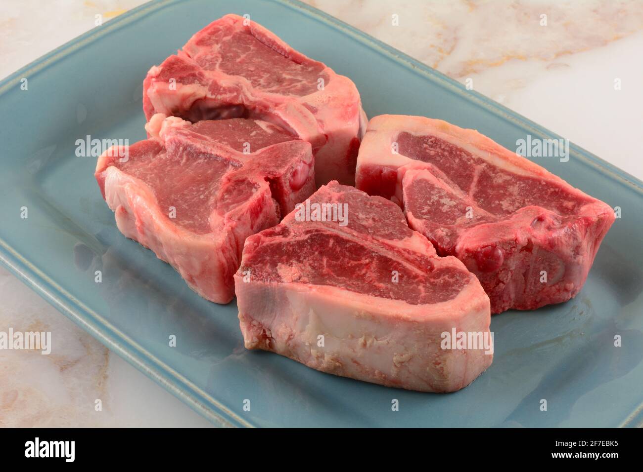Quattro costolette di agnello crude su piatto blu in preparazione per grigliare tostatura o cottura Foto Stock