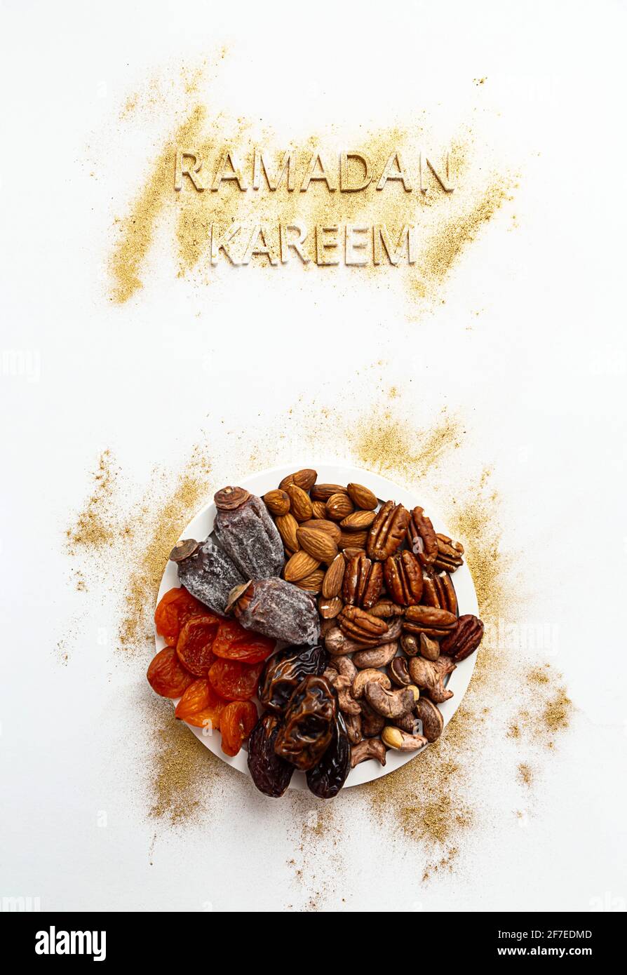 'Ramadan Kareem' e Iftar food, moderno concetto festivo in oro e bianco colori. Ramazan Kareem musulmano con date premium, noci, frutta secca. Foto Stock