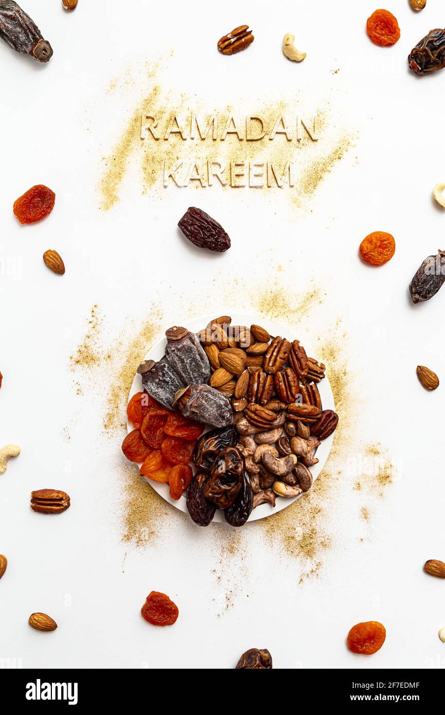 'Ramadan Kareem' e Iftar food, moderno concetto festivo in oro e bianco colori. Ramazan Kareem musulmano con date premium, noci, frutta secca. Foto Stock
