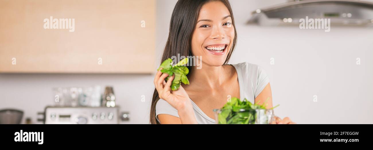 Cucina vegetale dieta sana donna mangiare foglie di spinaci a casa banner panoramico. Sorridente ragazza asiatica felice di fare la ricetta di succo verde. Foto Stock