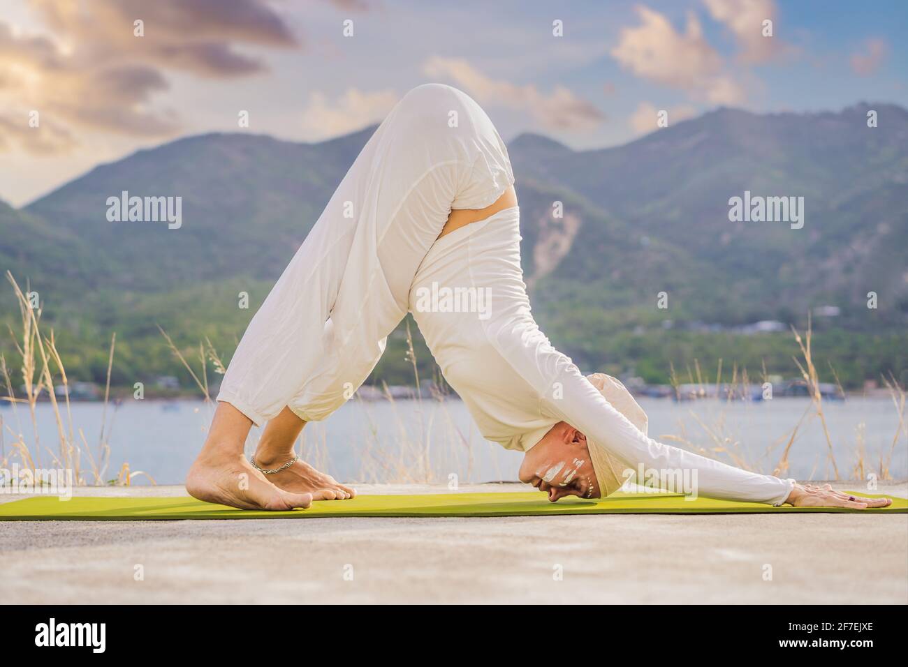 Kundalini yoga donna in abiti bianchi e turbani pratica yoga kundalini sullo sfondo del mare, le montagne e il tramonto. Pittura di faccia di combattimento Foto Stock