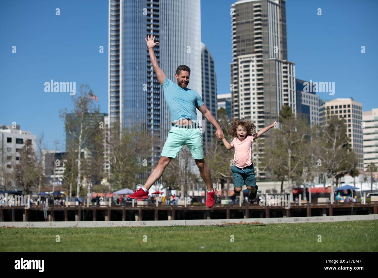 Divertente padre e figlio che saltano in città sullo sfondo. Concetto di bambino di infanzia e di paternità. Felice padre e figlio che giocano insieme all'aperto. Famiglie urbane. Foto Stock