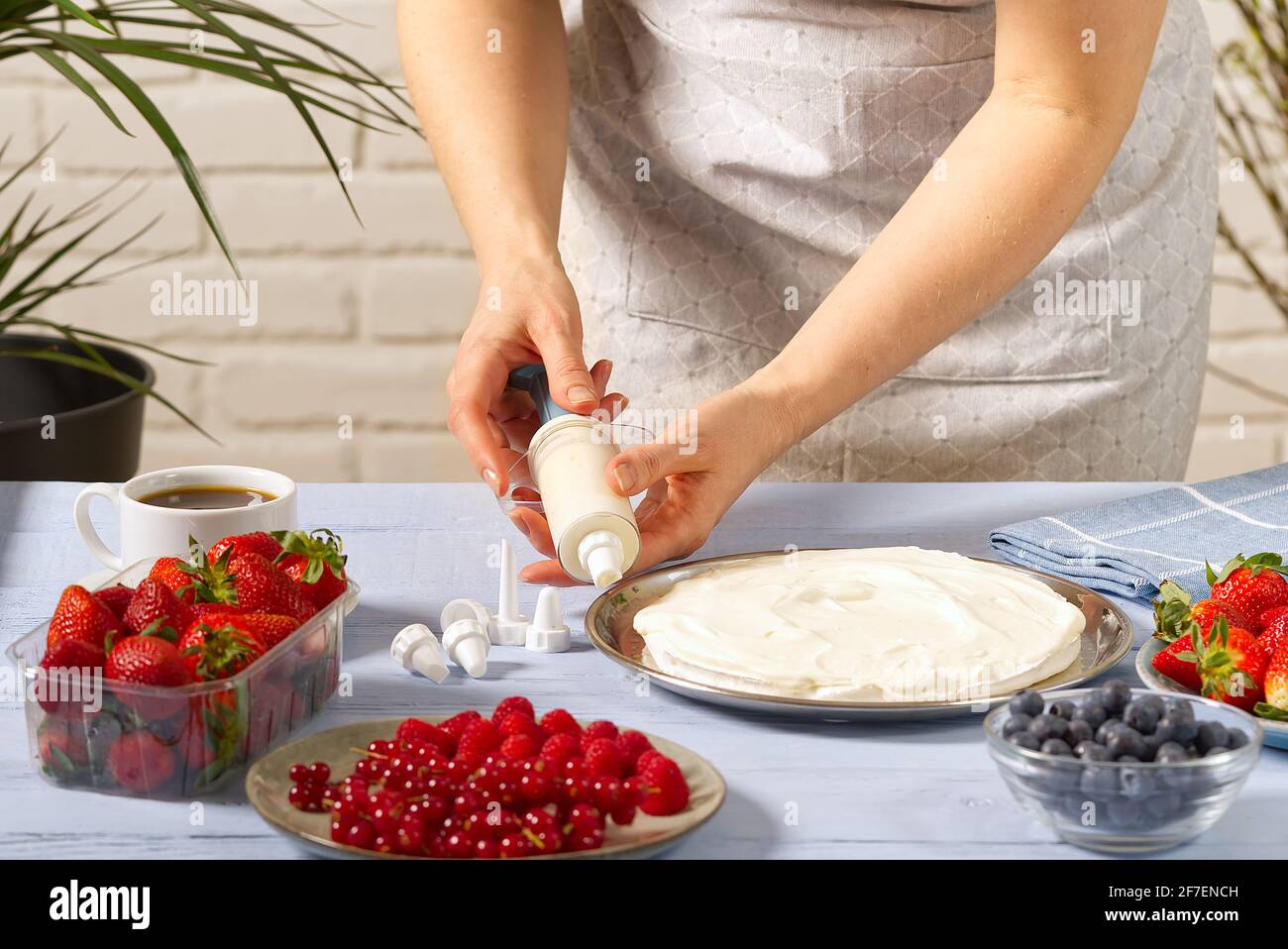 la panettiera donna strizza la panna montata. Torta di fragole fatta in casa con torta di meringa e crema con fragole. Foto Stock