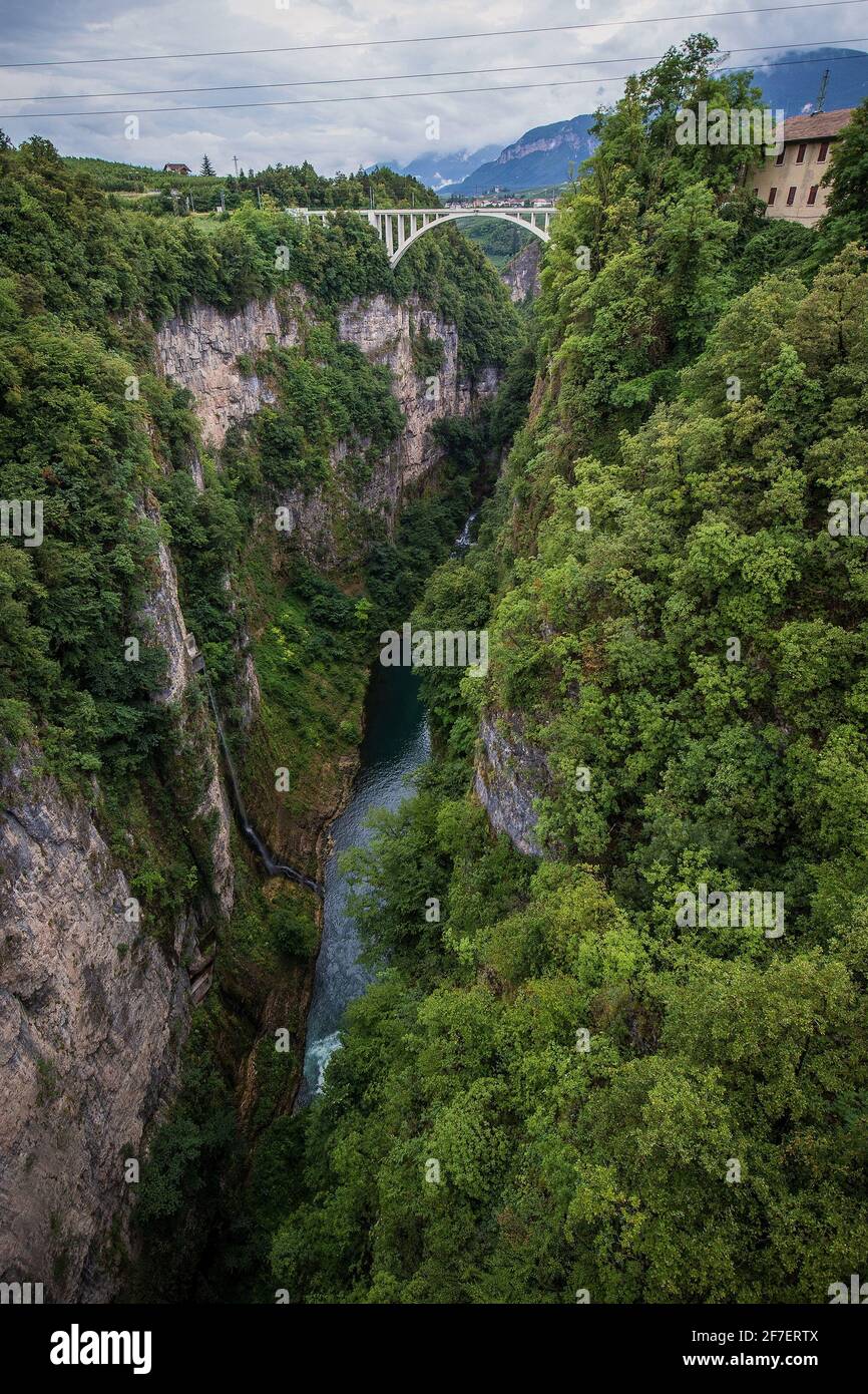 Profonda valle di gole con fiume Adige in fondo alle spalle della diga del lago Giustina in Italia, vicino alla città di Cles. Ponte ferroviario bianco visibile in Foto Stock