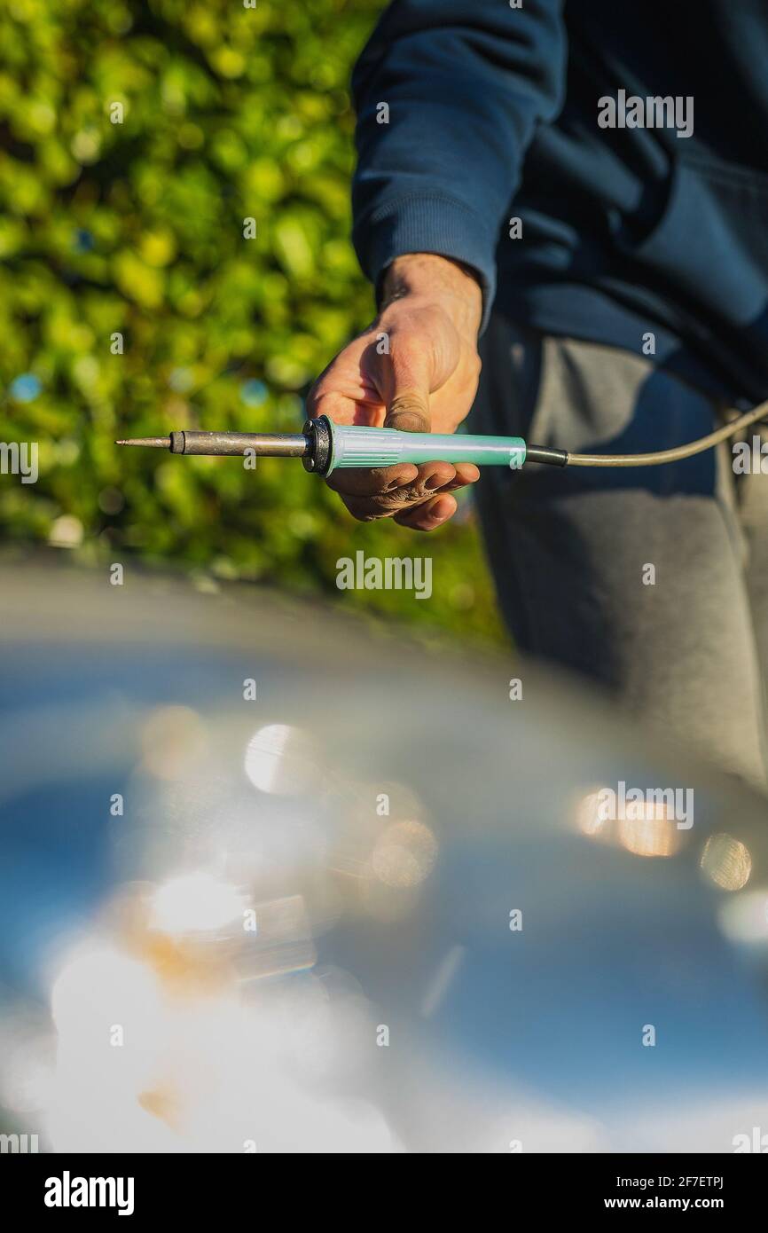 Man saldando i fili nel vano motore di un'auto. Auto moderna con riparazioni eseguite da un meccanico domestico. Caucasica che tiene una saldatrice professionale del filo. Foto Stock