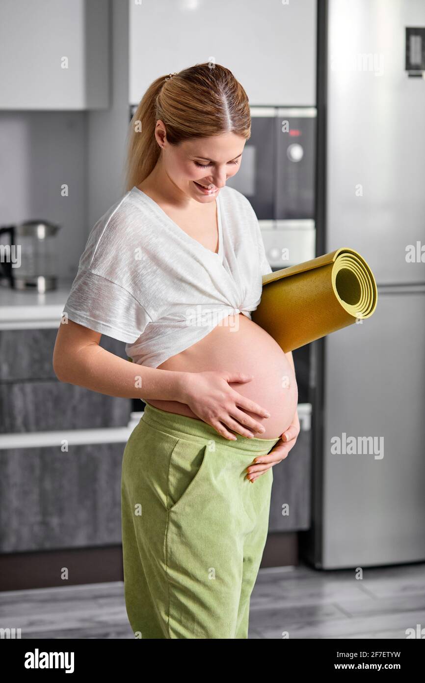 donna incinta in t-shirt bianca e pantaloni verdi in piedi, tummy hugging,  concetto di amore e gravidanza. ritratto di donna a casa, andare a pratica  Foto stock - Alamy