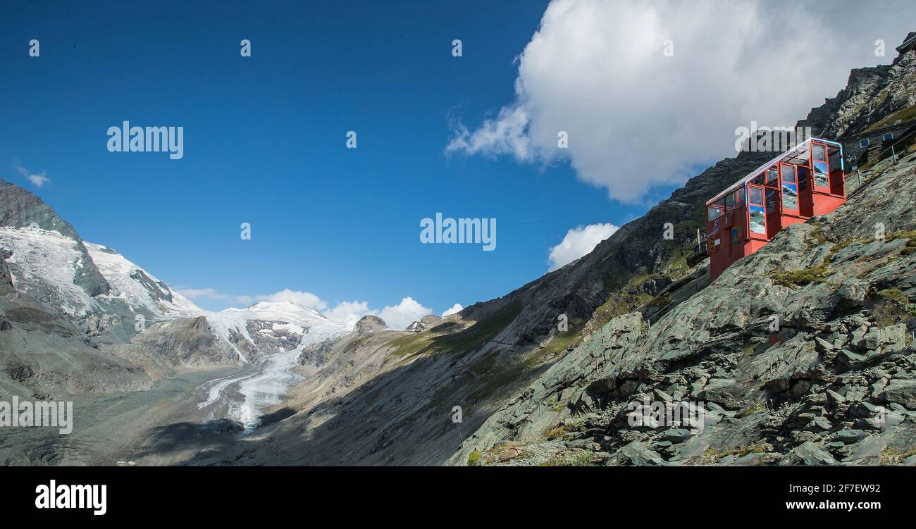 Funicolare rossa sulla catena montuosa del Grossglockner, proprio dietro il ghiacciaio Pasterze sullo sfondo in una calda giornata di sole con cielo blu in cima Foto Stock