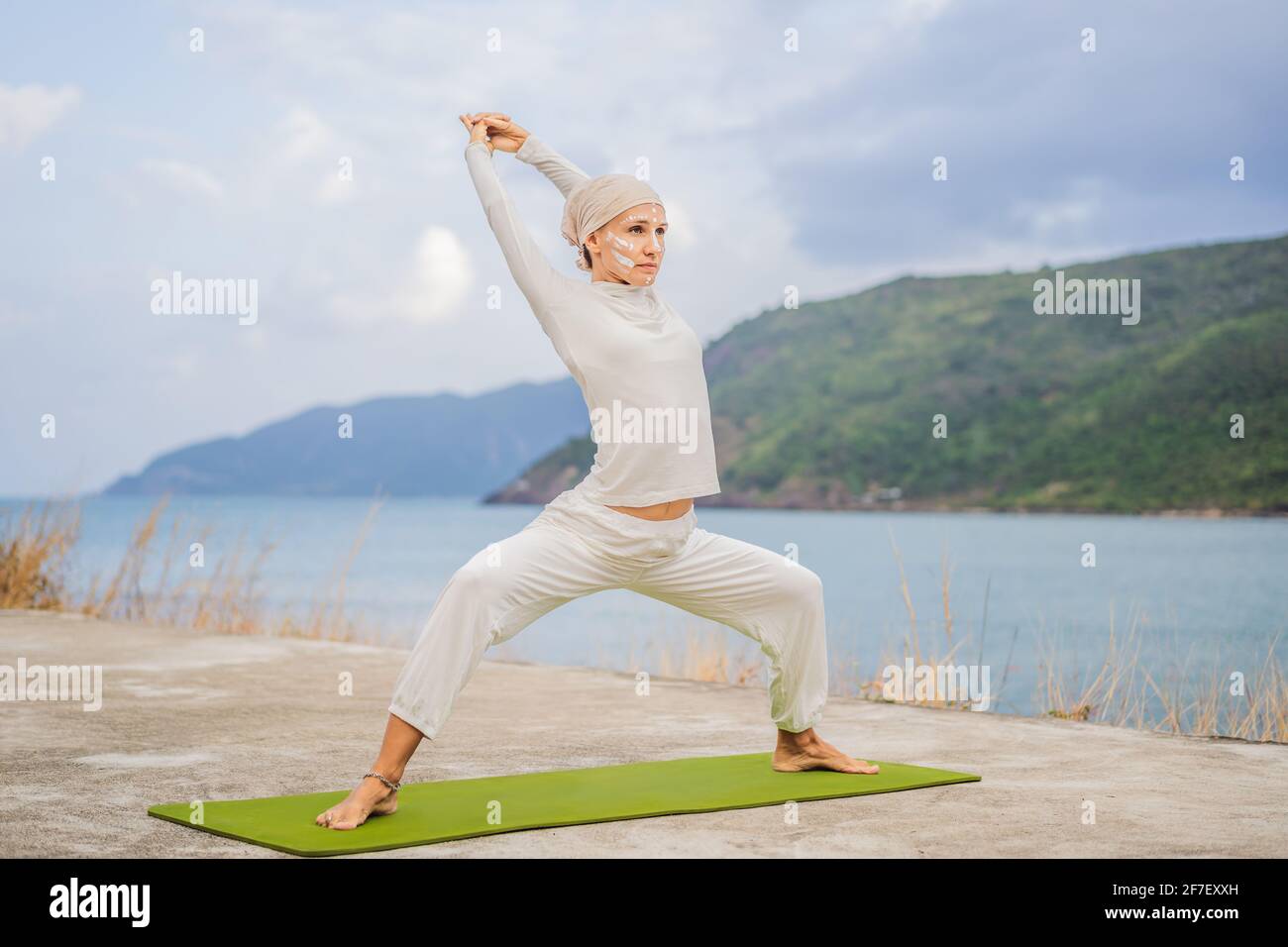 Kundalini yoga donna in abiti bianchi e turbani pratica yoga kundalini sullo sfondo del mare, le montagne e il tramonto. Pittura di faccia di combattimento Foto Stock