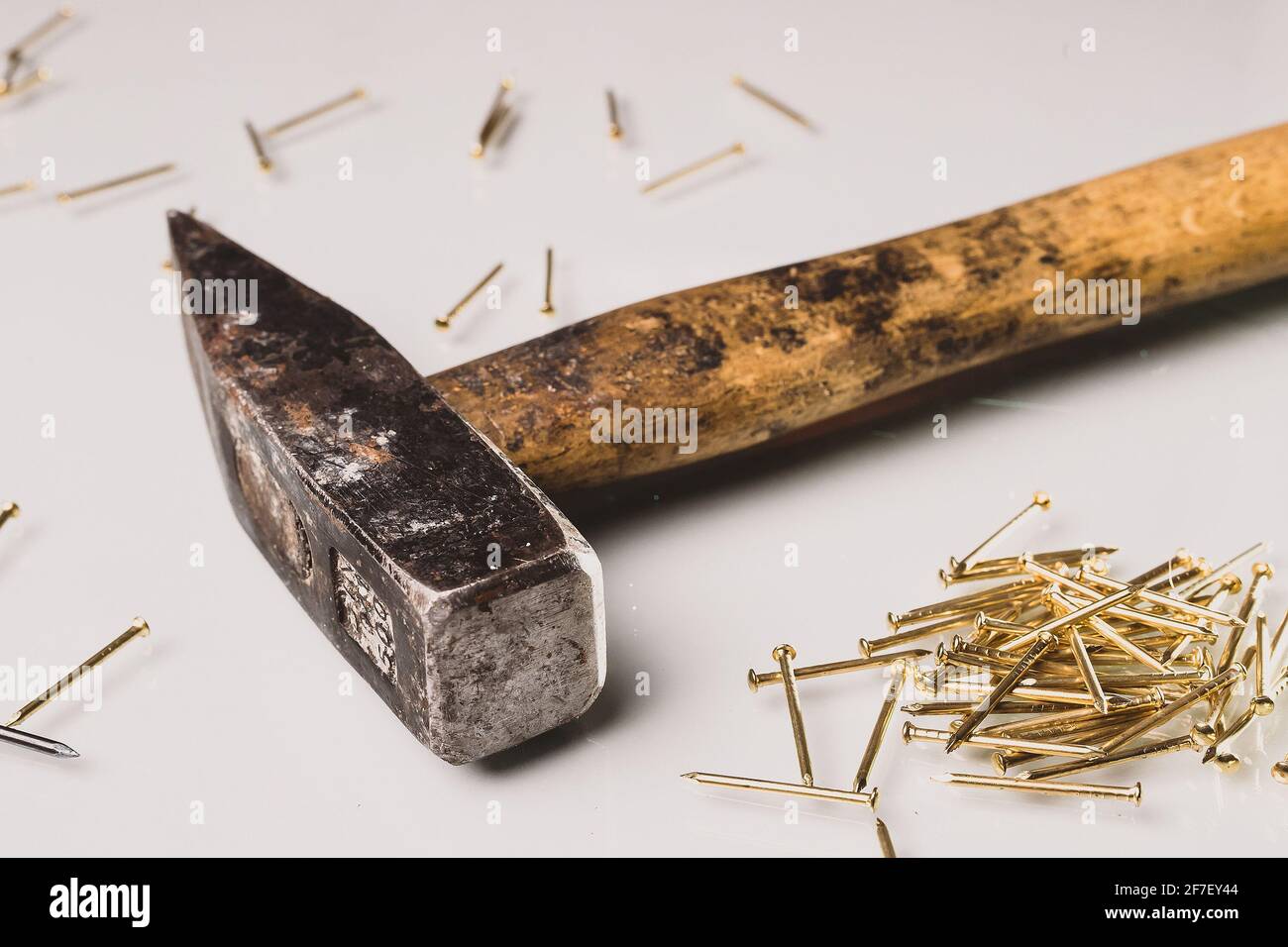 Un martello di stile europeo usato e usurato con manico in legno e punta in metallo e alcuni chiodi dorati. Isolato su scheda riflettente bianca. I chiodi dorati sono l Foto Stock