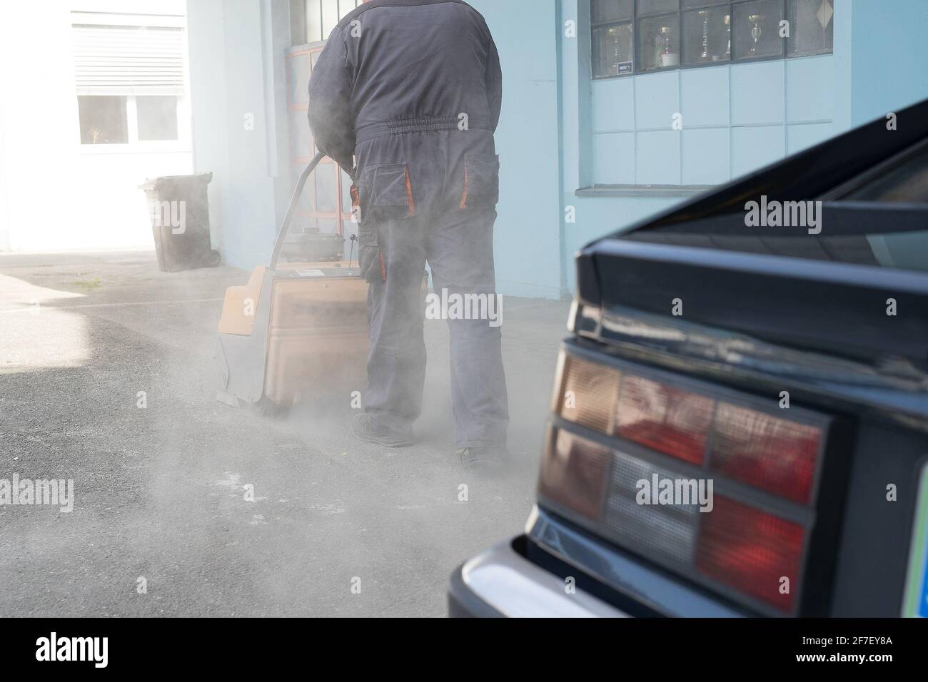 Una persona sta spingendo una spazzatrice industriale alimentata a benzina arancione parcheggio in asfalto sporco nel tentativo di pulire da detriti e sabbia Foto Stock