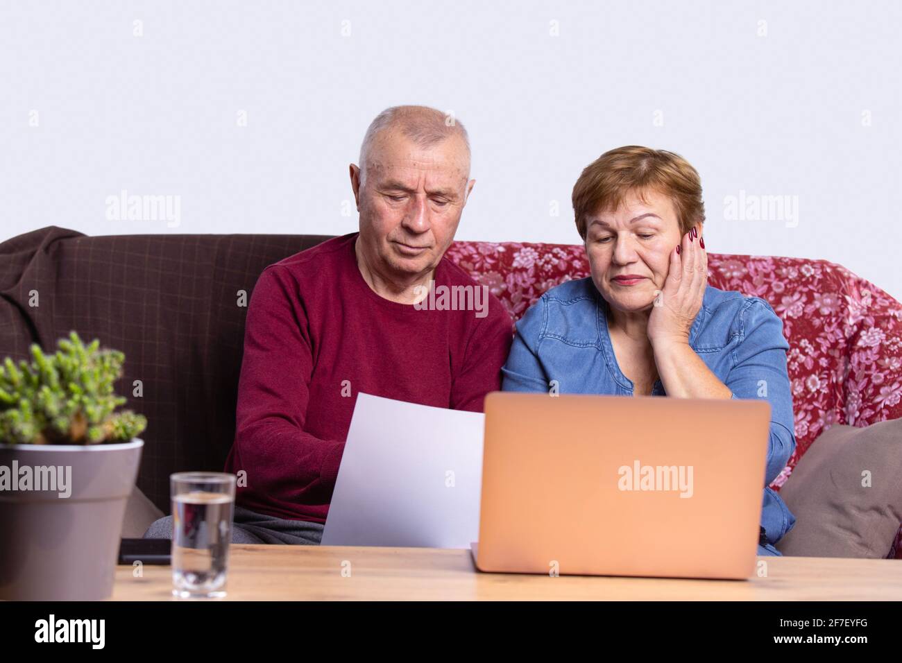 Coppia senior utilizzando computer portatile sul divano a casa per lo shopping online, navigare in internet, e-commerce, soggiorno, ufficio interno Foto Stock