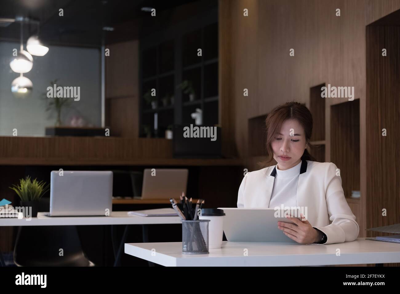 Giovane donna asiatica in tuta da lavoro che utilizza su tablet digitale nel suo ufficio Foto Stock