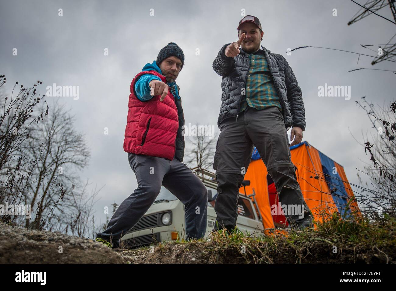 Due uomini in abiti sportivi all'aperto che si posano in natura durante il campeggio. Brokeback mountain stile moderno, una coppia divertente che punta a una macchina fotografica. Campervan in t Foto Stock