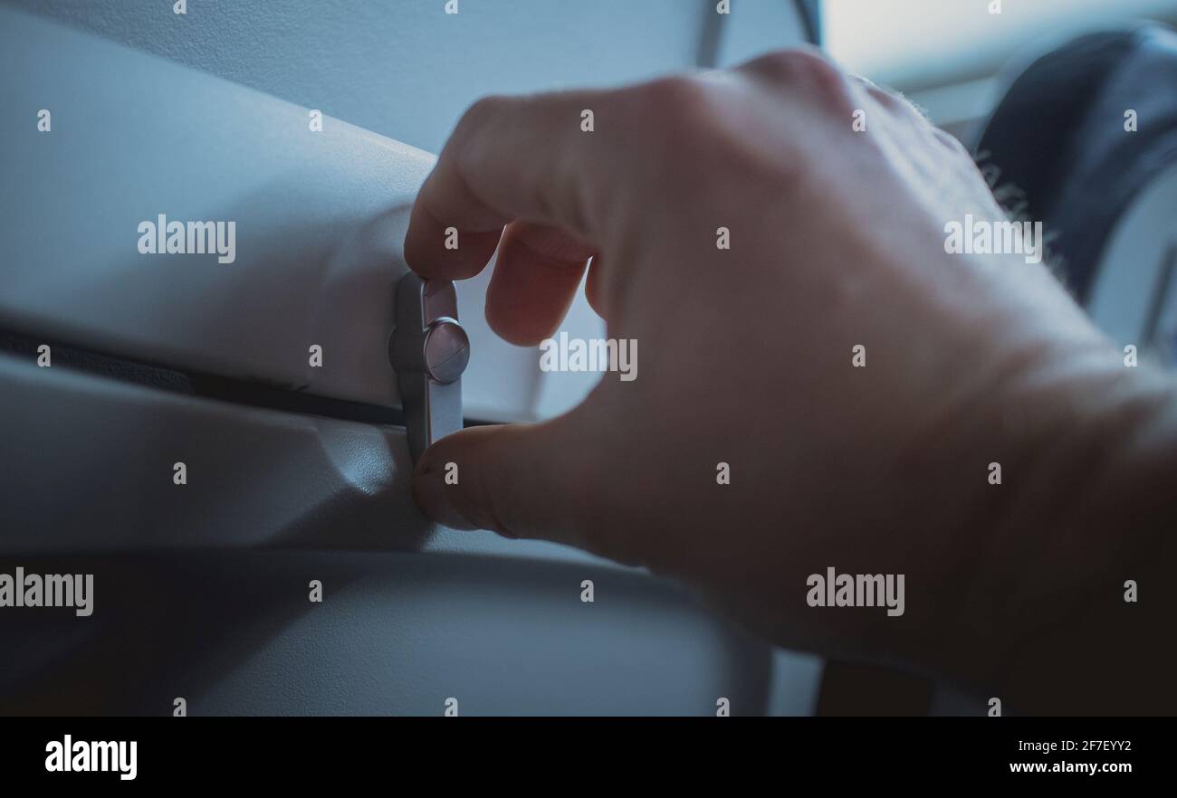 Manopola di apertura manuale per il rilascio del vassoio del tavolo sullo schienale di un sedile aereo. Vassoio visibile in posizione di stivaggio con una mano di una persona che ruota la manopola. Foto Stock