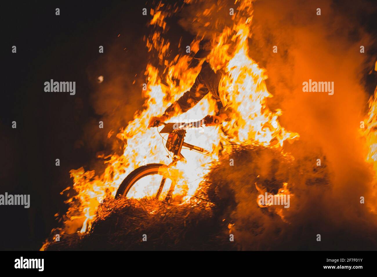 Ciclista completamente pazzesca su una mountain bike a cavallo tra falò, scintille e fiamme che sfrecciano oltre il biker in un evento reale. Biker pericolosamente giocare Foto Stock