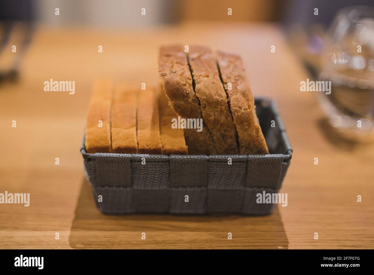 Fette di due diversi tipi di pane in un cesto di tessuto grigio su un tavolo di legno. Servendo con fantasia le fette di pane in profondità di campo poco profonda, concentratevi sul pane Foto Stock