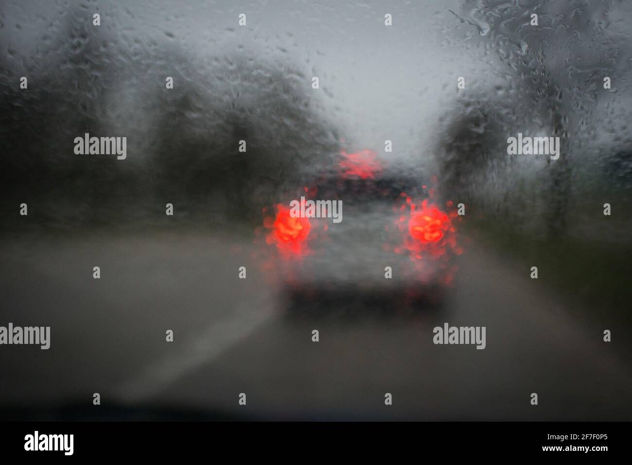 La pioggia cade sul parabrezza di un'auto impedendo una buona visibilità della frenata di un'auto davanti. Concetto di tempo di reazione ritardato dovuto al parabrezza sporco e piovoso. Foto Stock