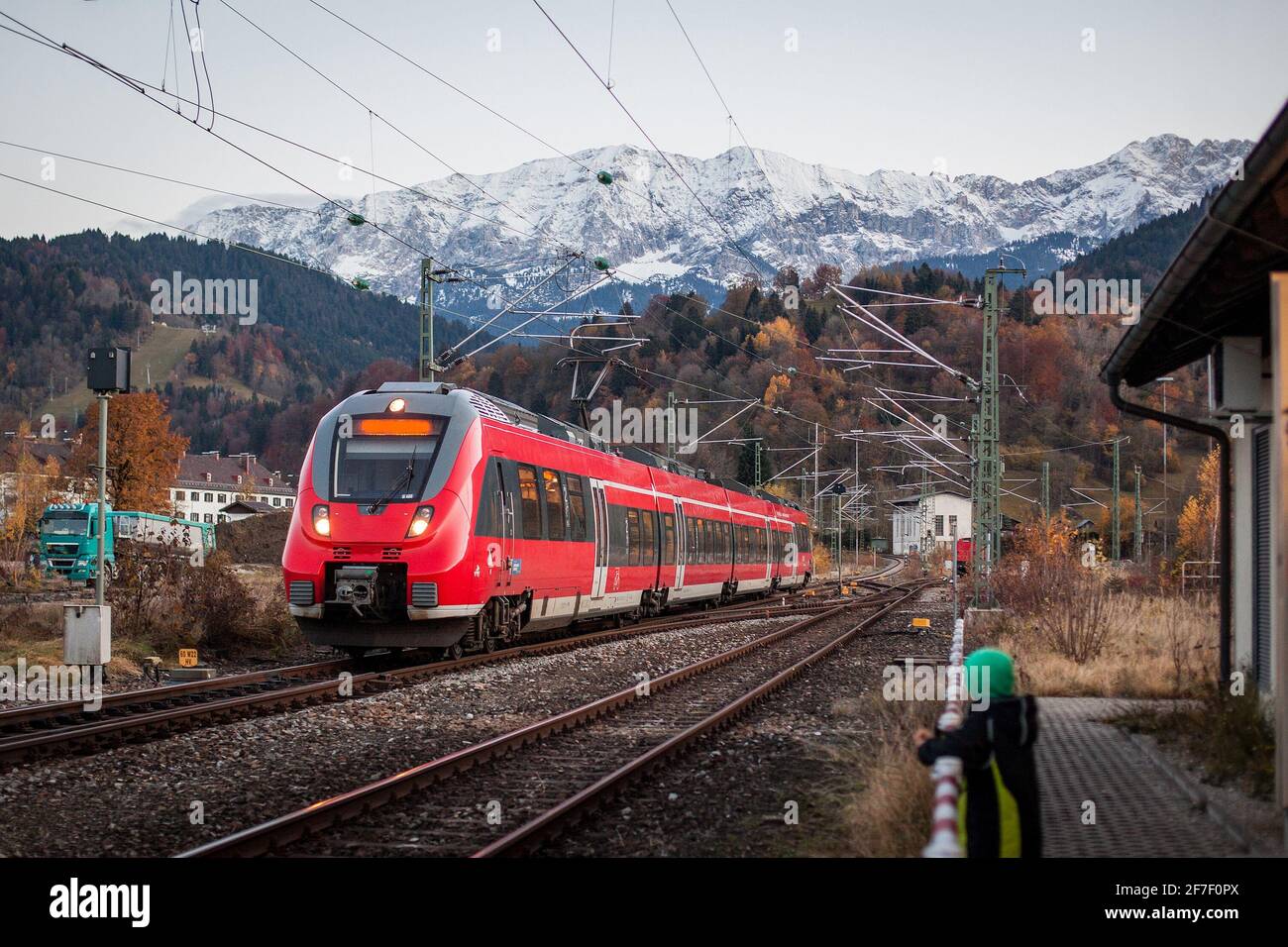 Il treno rosso per pendolari sta entrando in una stazione di Garmisch Partenkirchen nelle ore serali, con una fantastica vista di fondo sulle montagne e sulle colline innevate Foto Stock