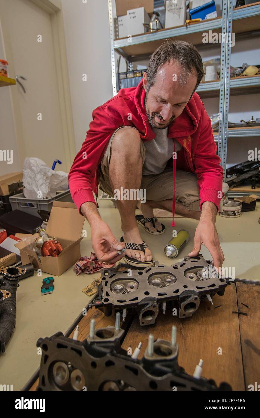 Un meccanico domestico che monta una testata V6 sul pavimento di un garage. Strumenti e parti diversi visti intorno. Foto Stock
