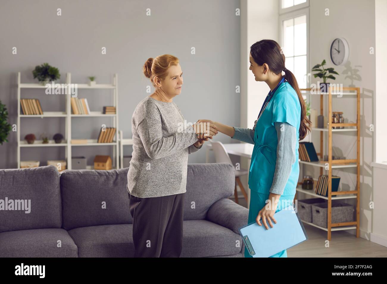 Paziente anziano scuotendo le mani con medico giovane ringraziandola per aiuto professionale Foto Stock