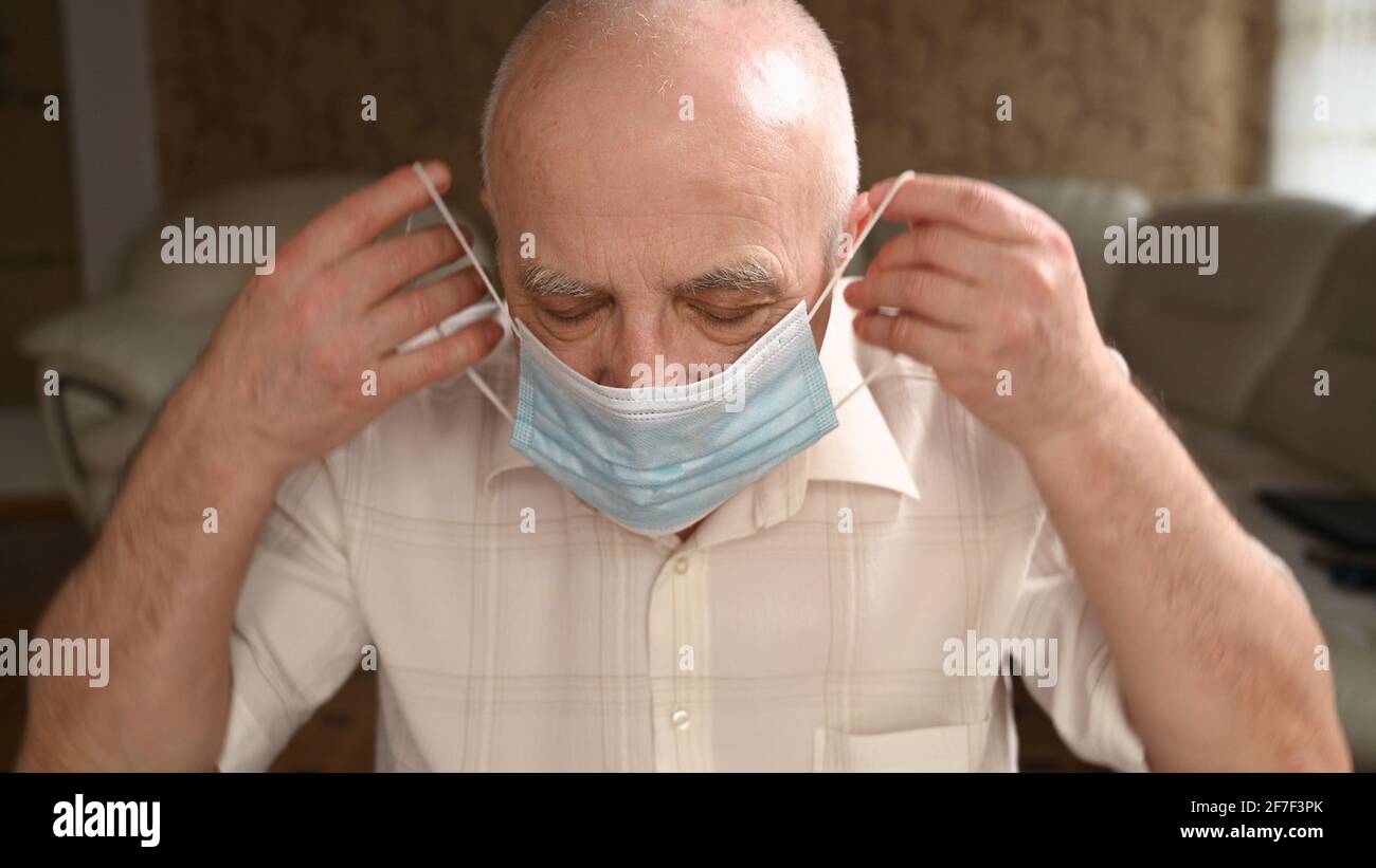 L'uomo anziano dai capelli grigi tira via la maschera protettiva. La pandemia finisce, difficoltà a respirare concetto Foto Stock