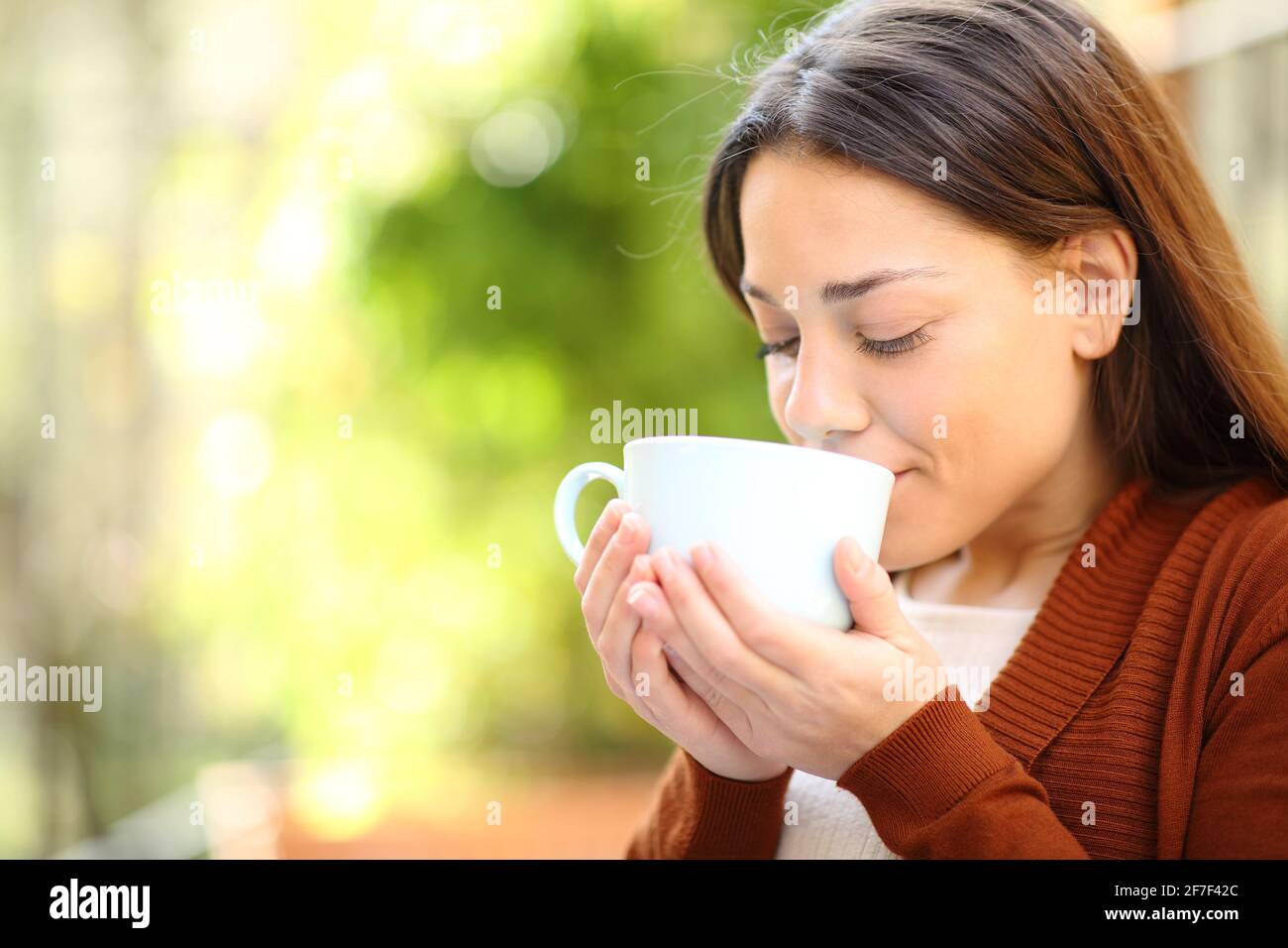Donna rilassata che beve caffè in un giardino verde casa Foto Stock
