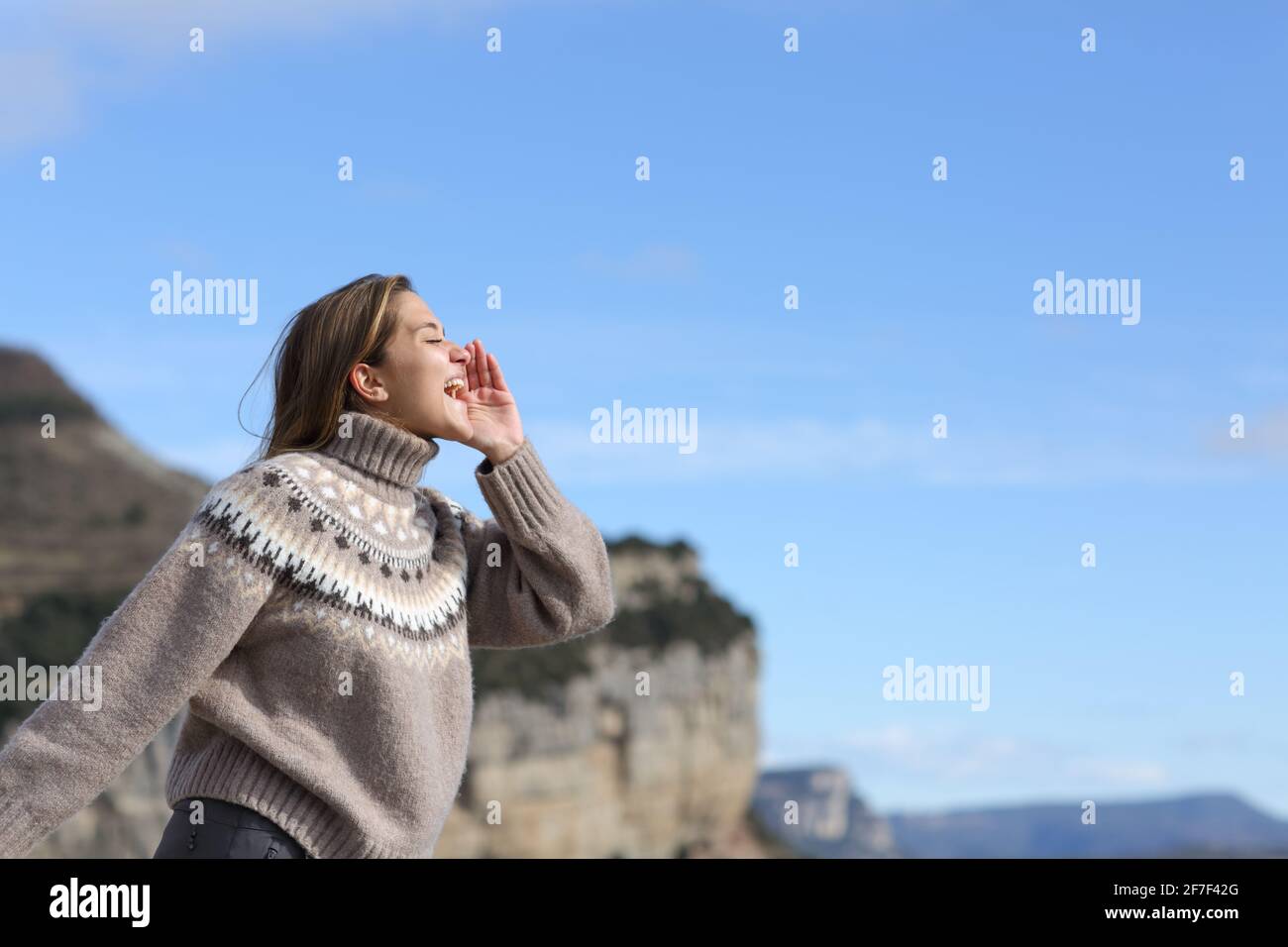 Vista laterale ritratto di una donna felice che grida di eco in montagna in inverno Foto Stock