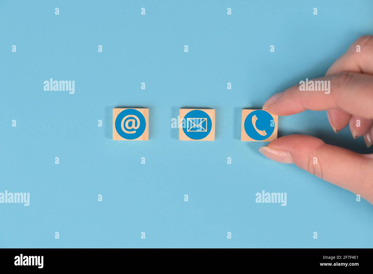 Mano che tiene cubi di legno con le icone di indirizzo di posta elettronica, telefono e sito web su sfondo blu. Informazioni di contatto, marketing e informazione. Foto Stock