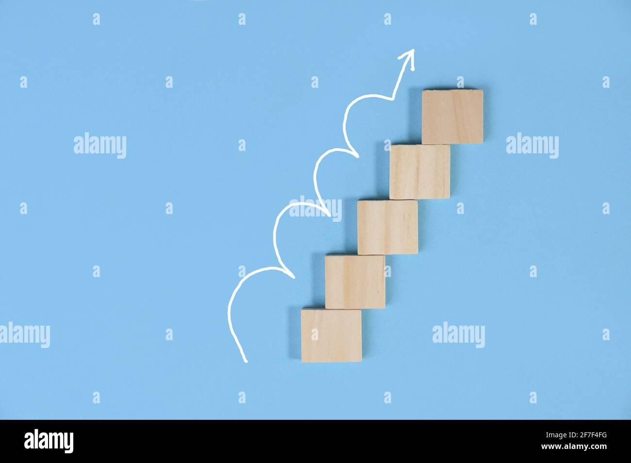 Blocco di legno impilato come scala con freccia bianca su isolato su sfondo blu pastello con spazio copia. Scala di successo nella crescita aziendale Foto Stock