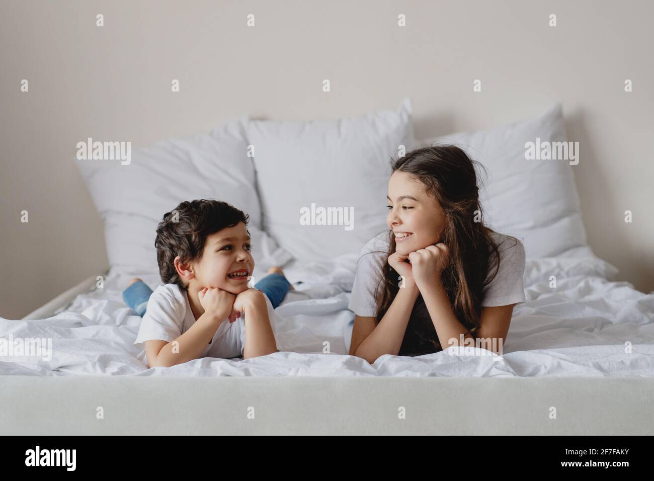 Fratello e sorella si aggirano sul letto sorridendo e guardandosi l'un l'altro. Foto Stock