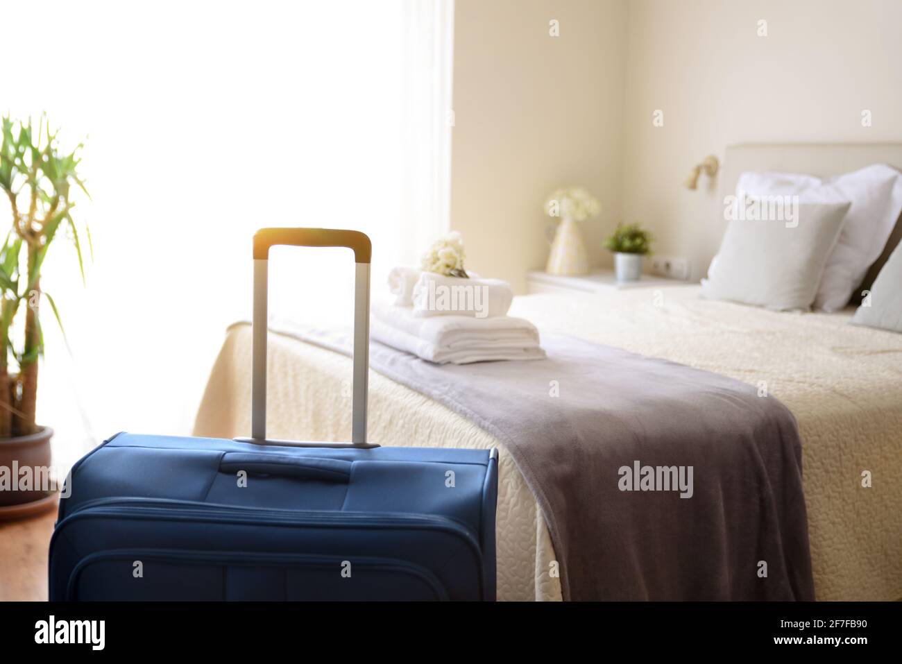Valigia in camera d'albergo molto luminosa con asciugamani bianchi puliti sul letto. Foto Stock