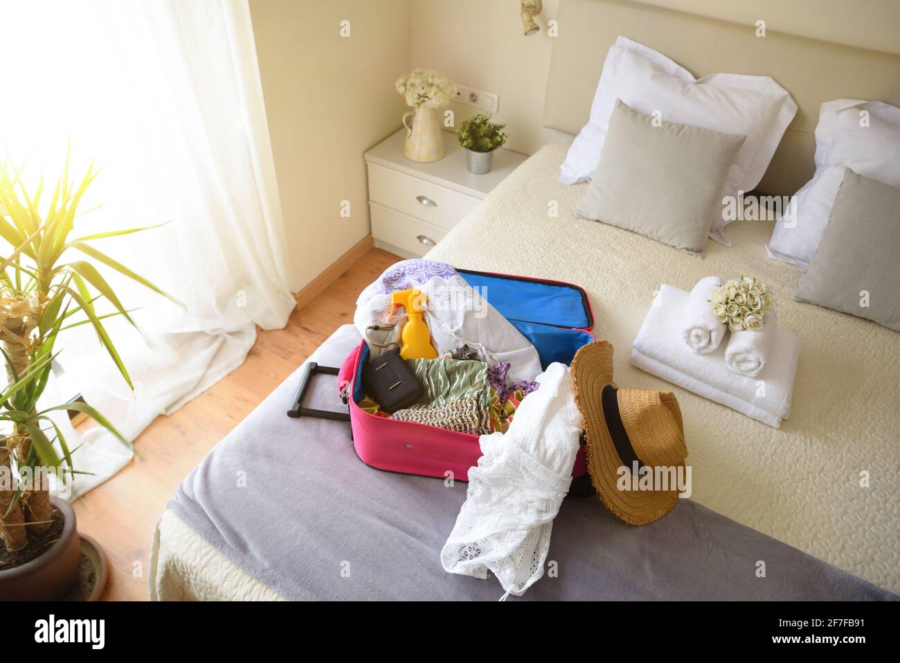 Valigia rosa aperta con abiti e oggetti per le vacanze da donna sul letto di una luminosa camera d'albergo. Vista dall'alto. Foto Stock