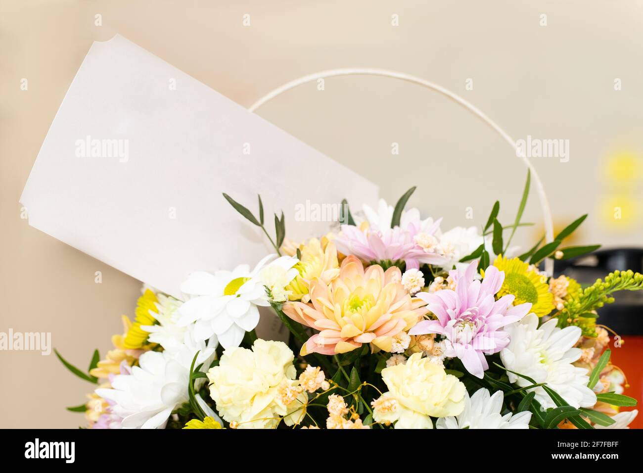 Bouquet di fiori rosa gialli bianchi con cartoncino bianco su sfondo chiaro e sfocato. Regalo o saluto inatteso. Corrispondenza segreta o invitatio Foto Stock