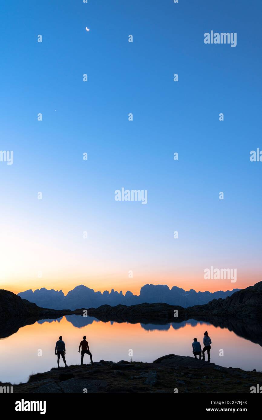 Escursionisti che ammirano le Dolomiti del Gruppo Brenta riflesse nel Lago Nero di Cornisello all'alba, Trento, Trentino-Alto Adige, Italia, Europa Foto Stock