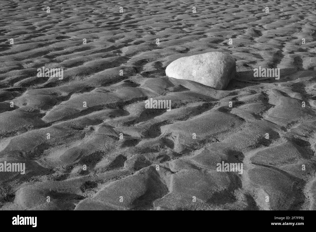 Una roccia sulla spiaggia tra le increspature della sabbia causate dalla marea in fase di recedimento. Foto Stock