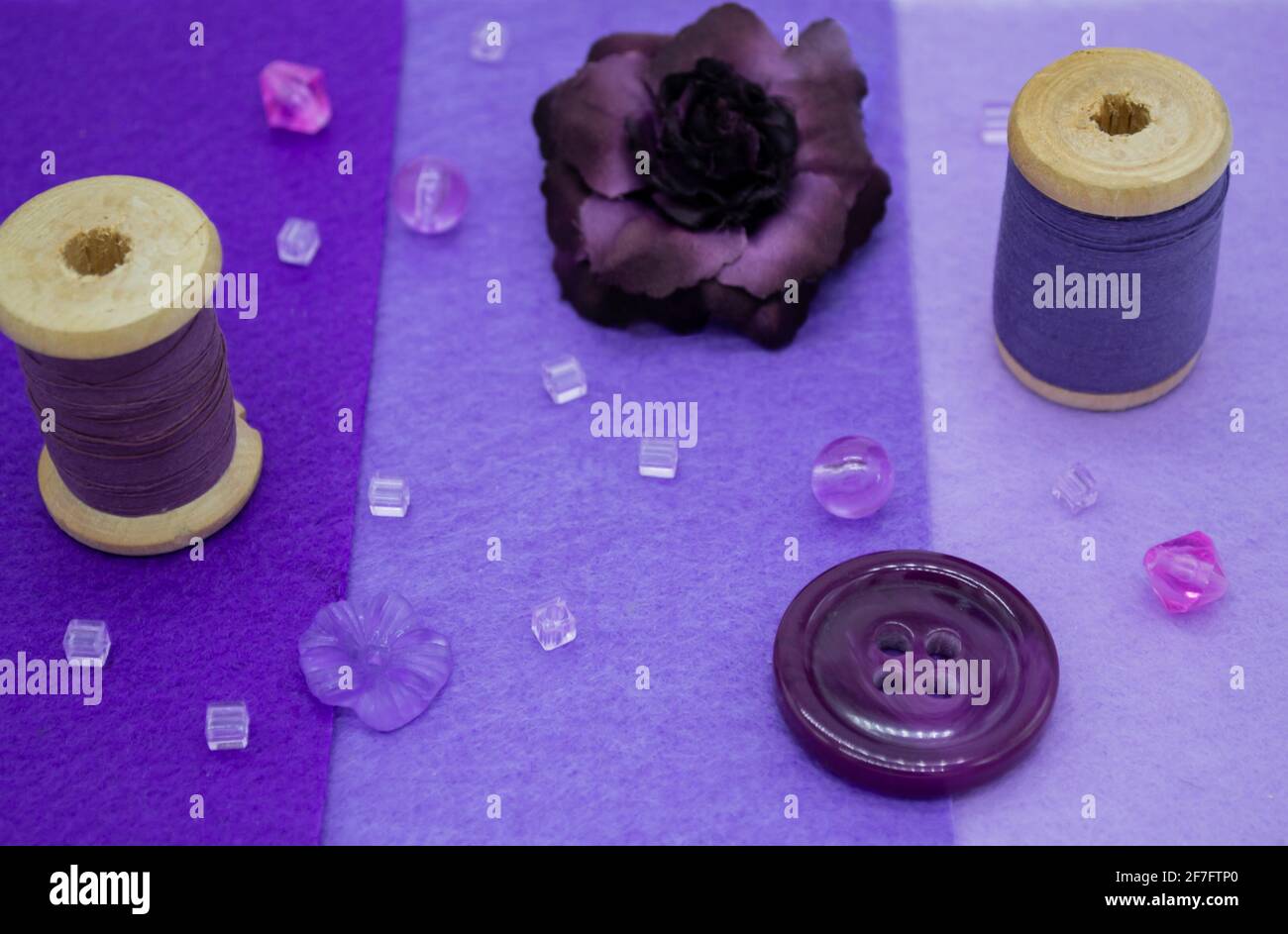Articoli da cucire viola: Feltro in tre tonalità di lilla, bobine di legno con filo, perline, bottoni, e una rosa viola. Foto Stock