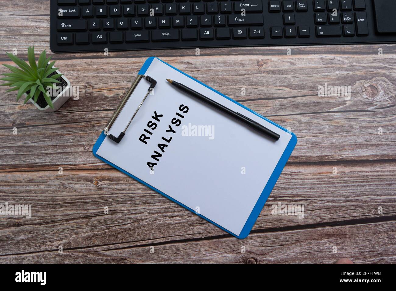 Testo di analisi del rischio su clipboard blu con tastiera, penna e pianta in vaso Foto Stock
