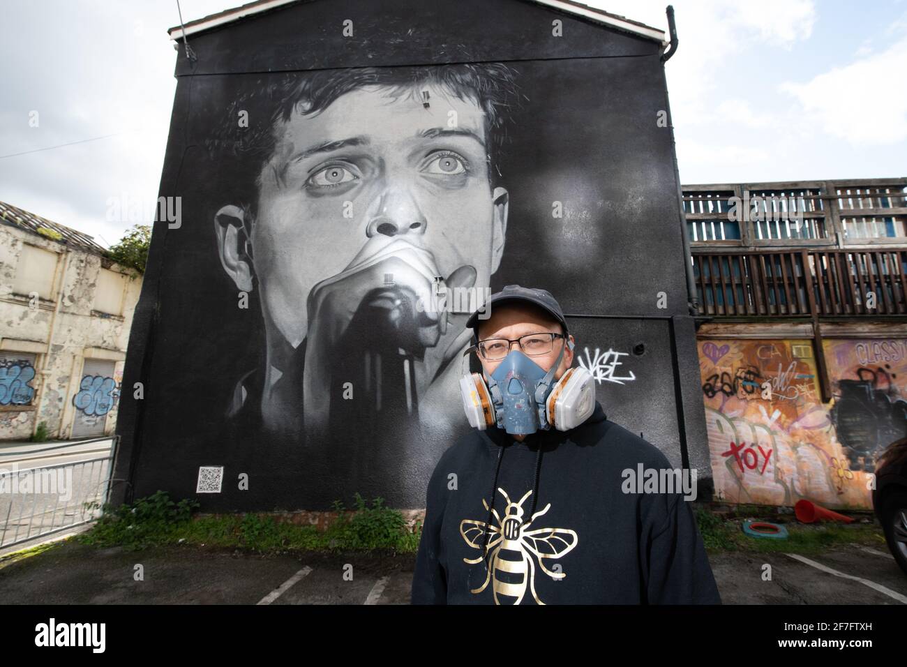 Akse, artista di strada, si trova di fronte al murale del frontman di Joy Division, Ian Curtis. Foto Stock