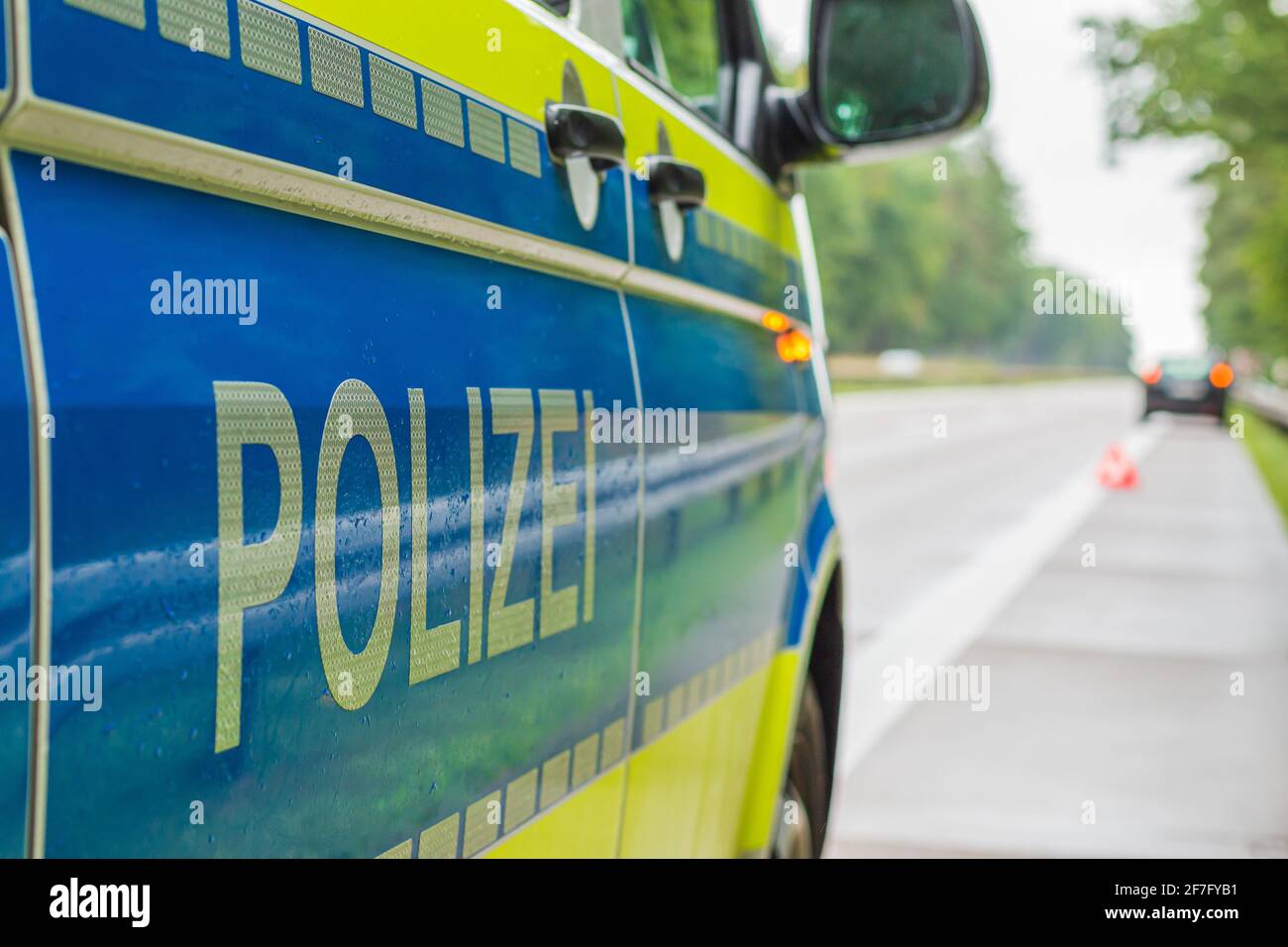 Ammira un'auto della polizia tedesca sull'autostrada. Scritta sul corpo con strisce riflettenti su sfondo blu e giallo. Piste piovose e alberi. Foto Stock