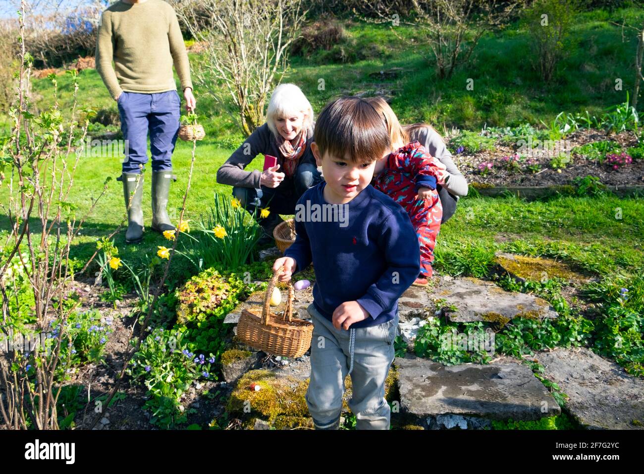 Bambino felice con i genitori e la nonna sull'uovo di Pasqua della famiglia Caccia detenere cestino caccia per uova nel giardino primaverile Galles REGNO UNITO KATHY DEWITT Foto Stock