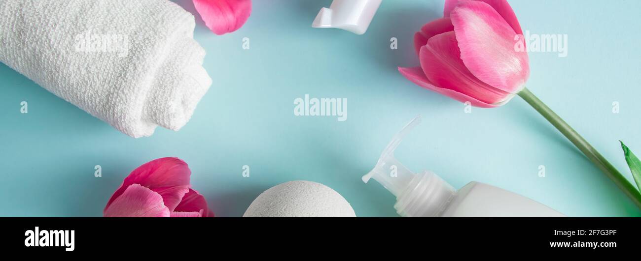 Prodotti per la cura della pelle su sfondo blu. Cosmetici naturali e tulipani rosa. Posiziona per testo, formato banner Foto Stock