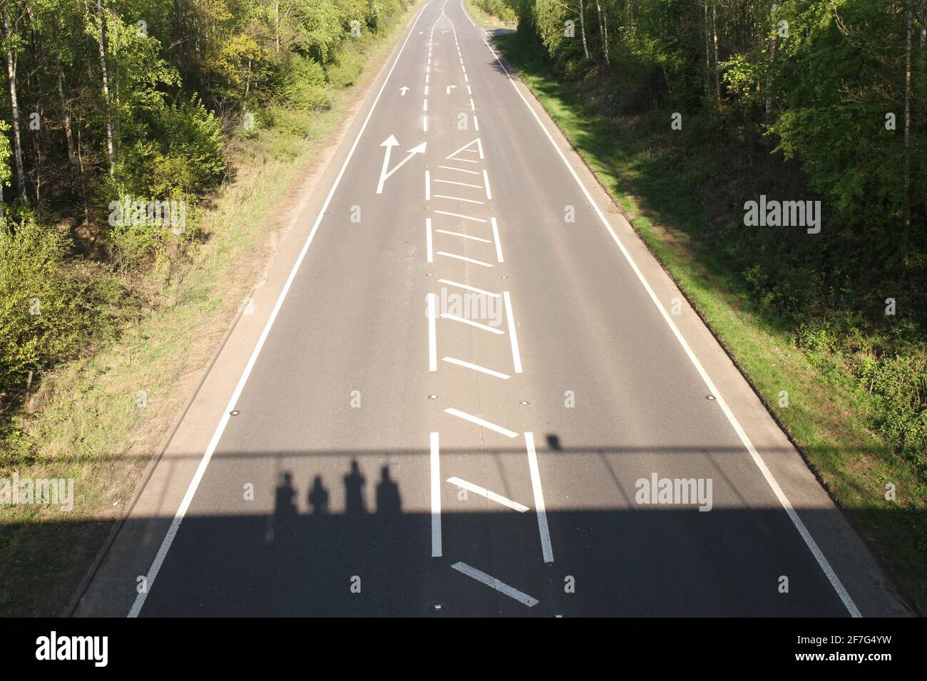 Empty Main Road senza traffico durante il Lockdown nel Regno Unito, con 4 Shadows of People in piedi su un ponte pedonale, oltre la strada. Foto Stock