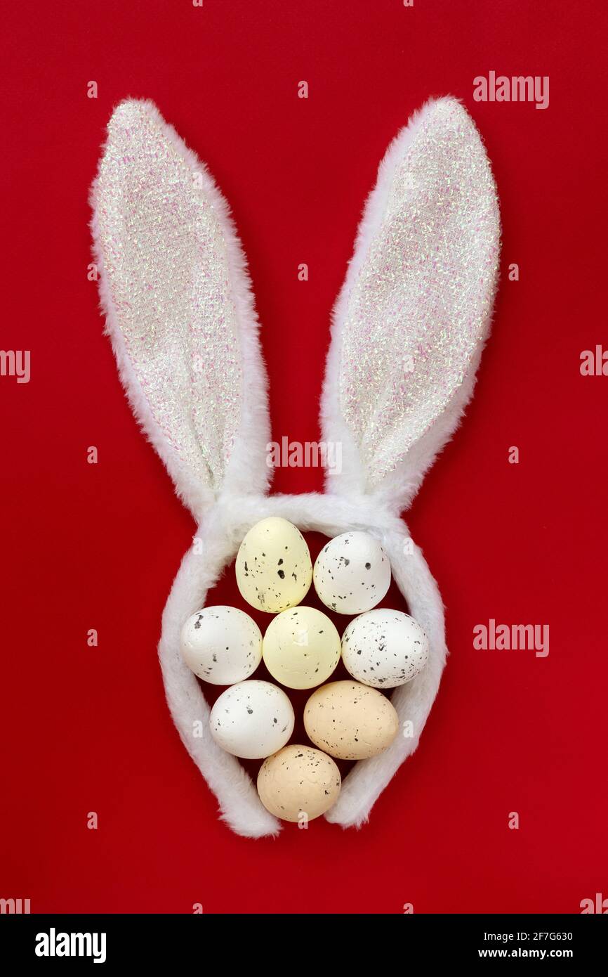 Fiaccie orecchie conigliate con uova di Pasqua colorate isolate su sfondo rosso, vista dall'alto, piatto. Foto Stock