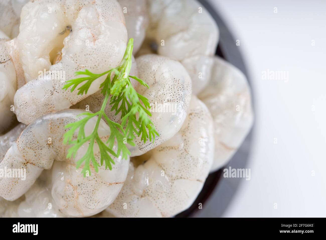 Gamberi o gamberetti pelati grezzi disposti in ceramica nera pentola piccola e guarnita con foglia di coriandolo che è pronta per cucinare, messo su un bianco testurizzato Foto Stock