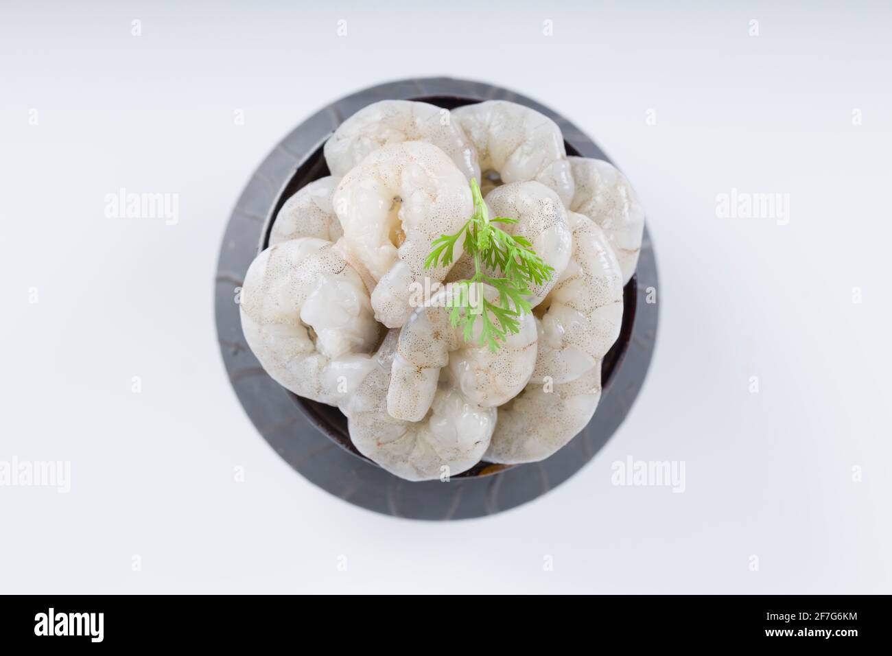Gamberi o gamberetti pelati grezzi disposti in ceramica nera pentola piccola e guarnita con foglia di coriandolo che è pronta per cucinare, messo su un bianco testurizzato Foto Stock