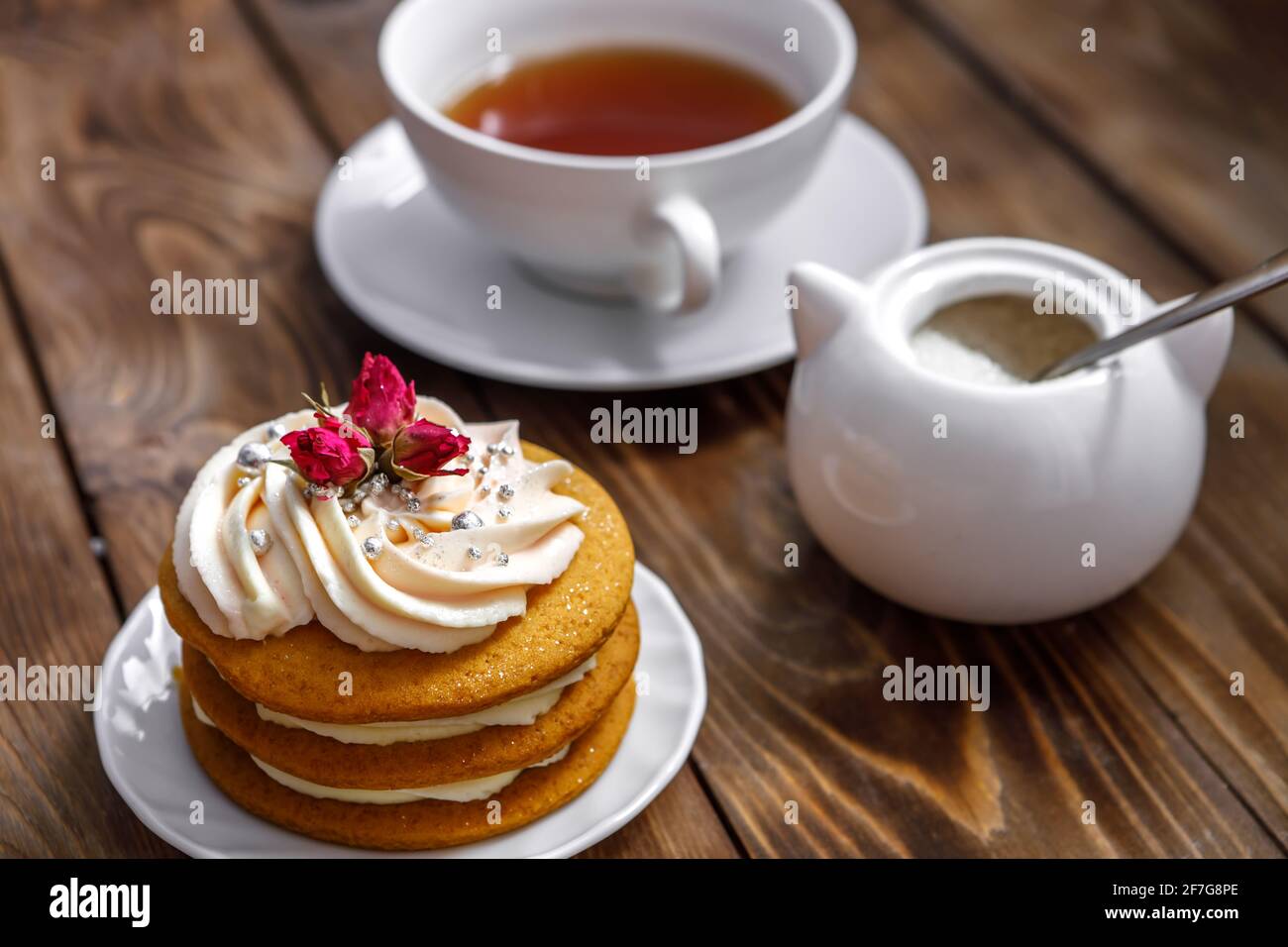Pan di Spagna con panna, decorato con fiori piccoli e una tazza di tè. Il concetto di un piacere di festa. Lavoro fatto a mano Foto Stock
